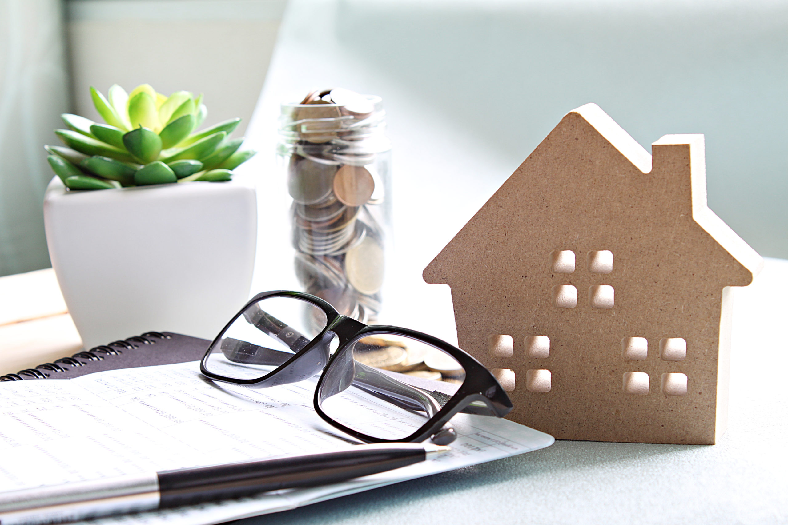 Wood house model, coins, eyeglasses and saving account book or financial statement on office desk table Wood house model, coins, eyeglasses and saving account book or financial statement on office desk table