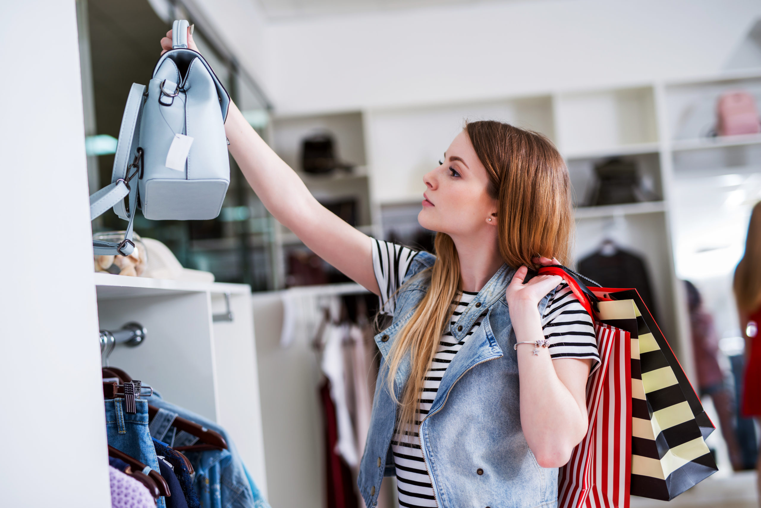 Young female shopper with shopping bags choosing the handbag matching her casual style Young female shopper with shopping bags choosing the handbag matching her casual style