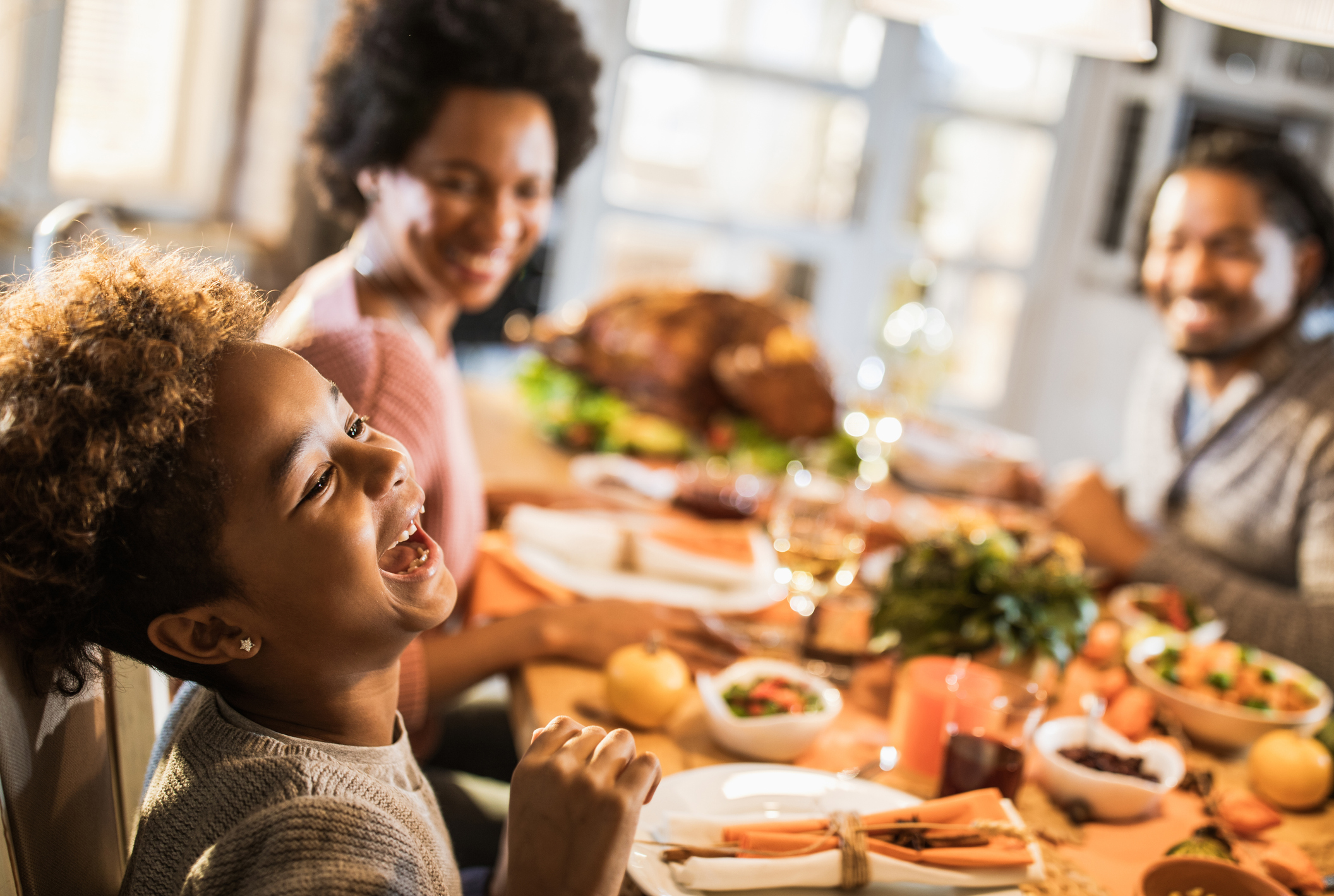 Cheerful African American girl with her parents at dining table.